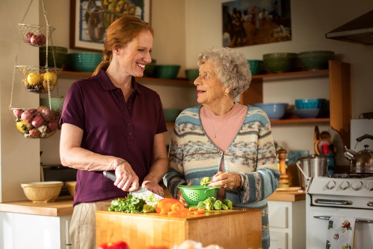 A caregiver and an older woman preparing vegetables together in a warm home kitchen