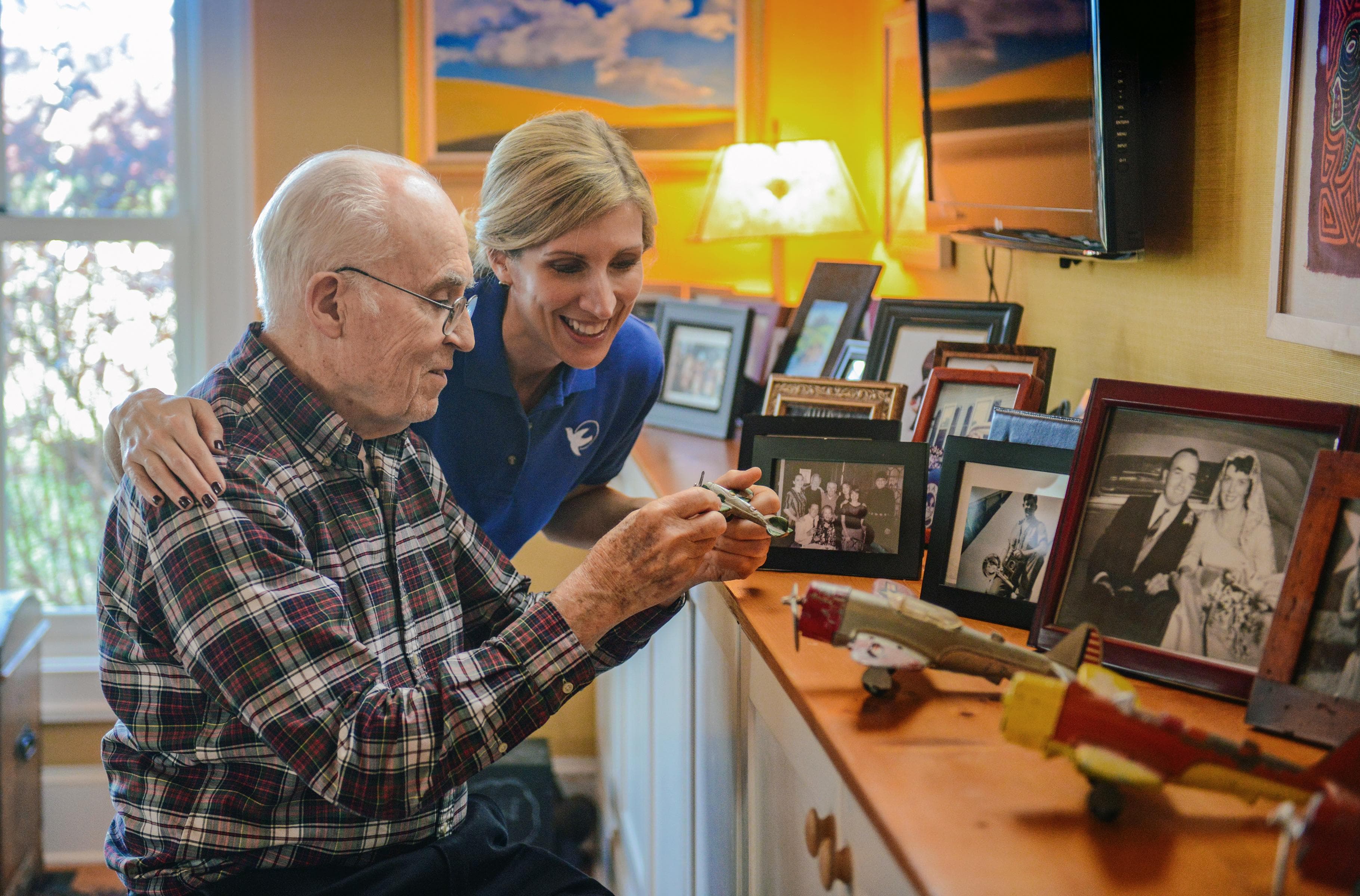 A caregiver and an older man looking together at his model airplanes and family photographs