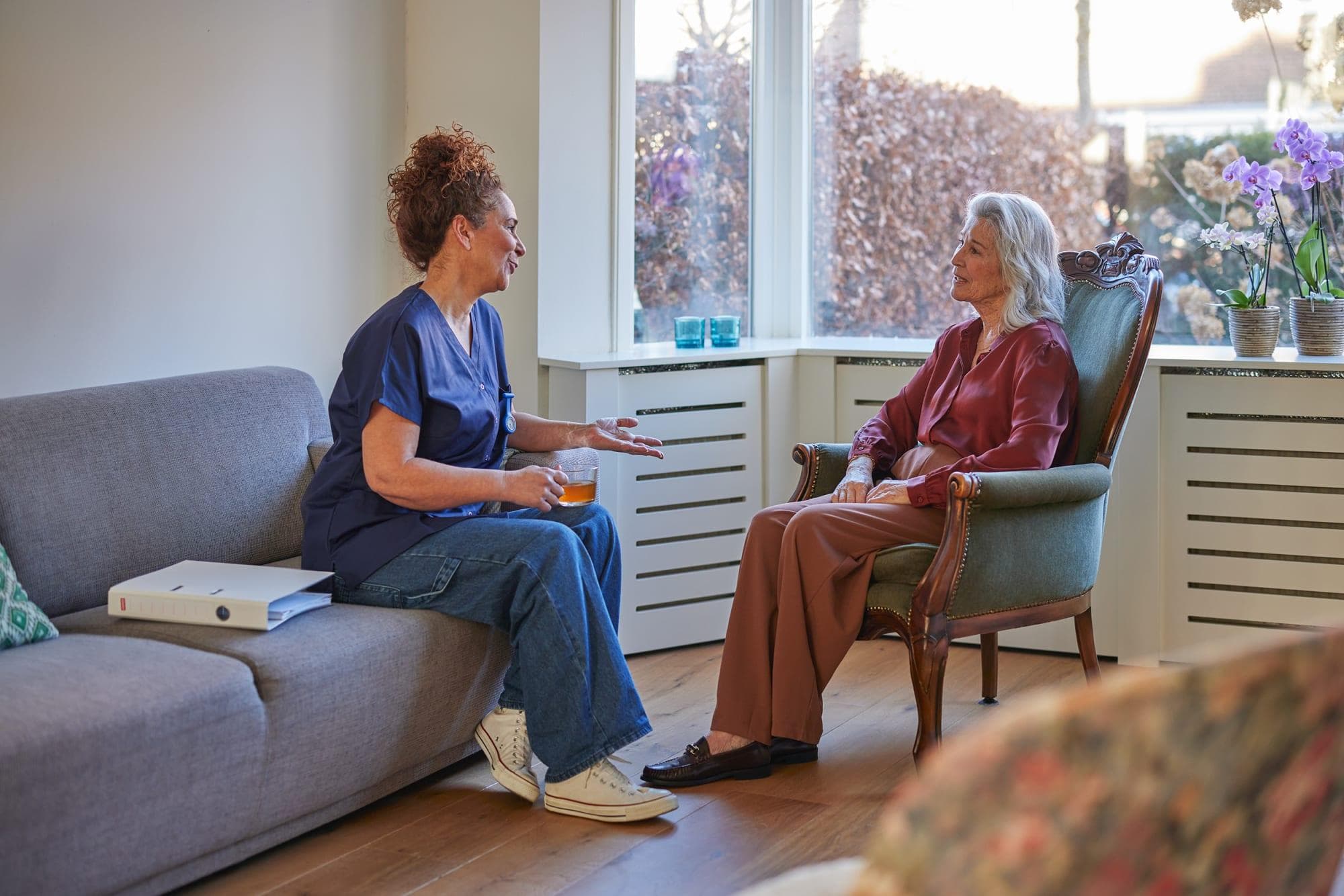 A care coordinator and an older woman talking comfortably by a sunny window
